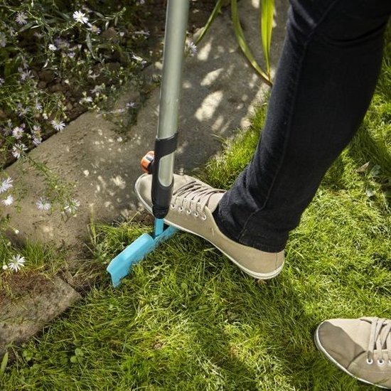 Persoon met bruine schoenen gebruikt de turquoise graskantafsteker op gras bij een stenen rand.