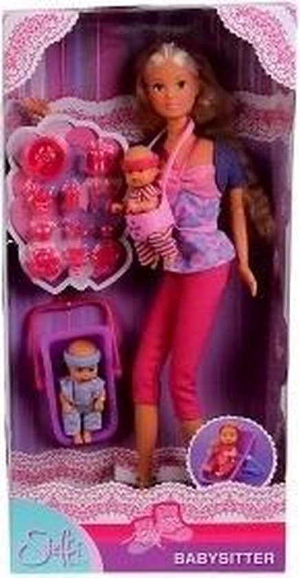 Doos van Steffi Love babysitter pop met roze en paarse kleding. Ze draagt een baby in draagzak en houdt wiegje met baby.