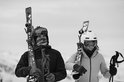 Man en vrouw in skikleding met ski's en helmen, beiden dragen nekwarmers met abstracte print.