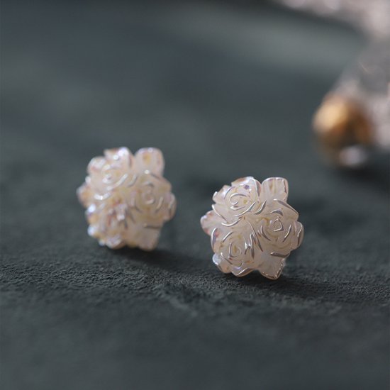 Witte bloem-vormige oorknoppen met parelmoerglans, gedetailleerde blaadjes, op een donkergroene achtergrond.