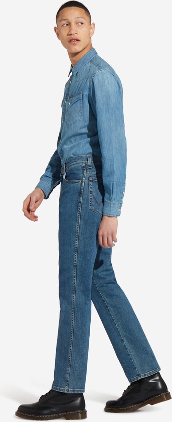 Man, lopend, draagt een blauwe spijkerbroek, denim overhemd en zwarte schoenen, zijaanzicht.