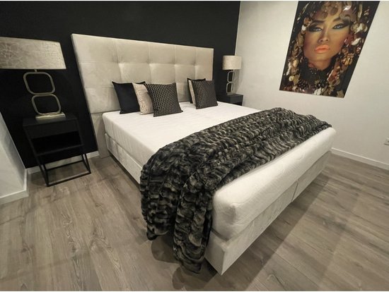 Chique slaapkamer met beige boxspring, vier kussens, sprei, twee nachtkastjes met lampen en een schilderij.