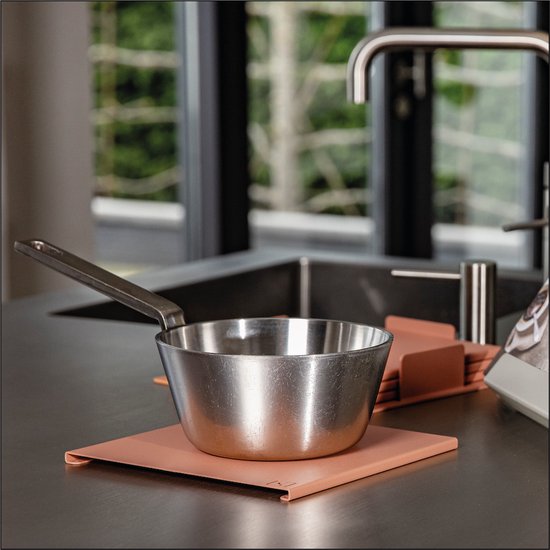 Lichtroze onderzetters op een aanrecht met een pan, met een metalen kraan op de achtergrond.