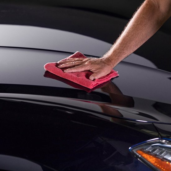 Main polissant le capot brillant d'une voiture foncée avec un chiffon rouge.