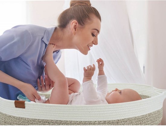 Moeder die lacht naar baby in beige touwen wieg.
