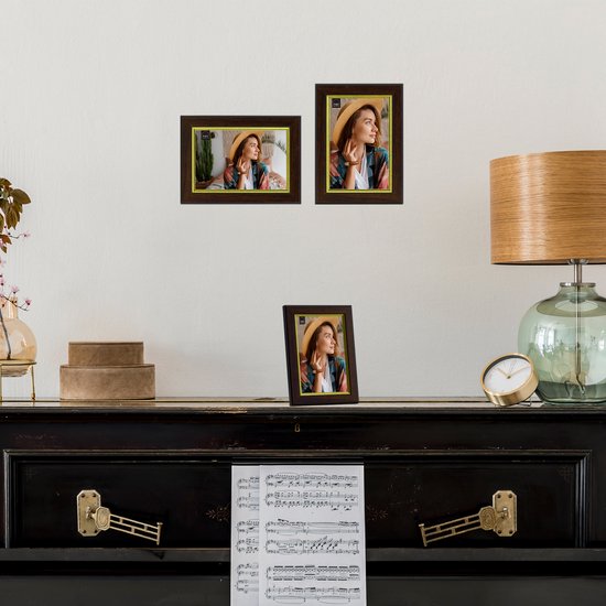 Drie bruine fotolijsten met gouden rand op een witte muur boven een piano.