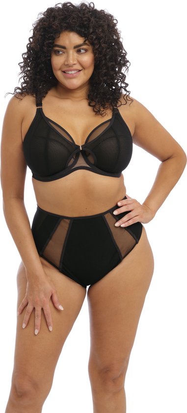 Model met krullend haar in een zwarte plunge beha en hoge bikinislip met mesh inzetstukken, posant op een witte achtergrond.