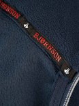 Detail van een zwarte band met rode tekst 'BJØRNSON' en witte logo's op een donkerblauwe fleece jas.