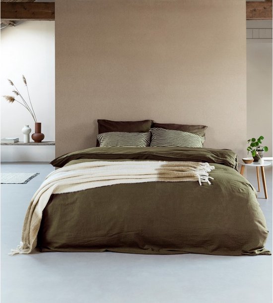 Lit fait avec une couette vert foncé, des oreillers rayés et un jeté de lit beige à franges.