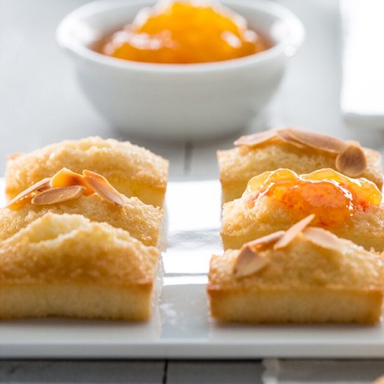 Vier kleine gouden gebakjes gegarneerd met amandelschilfers en jam.