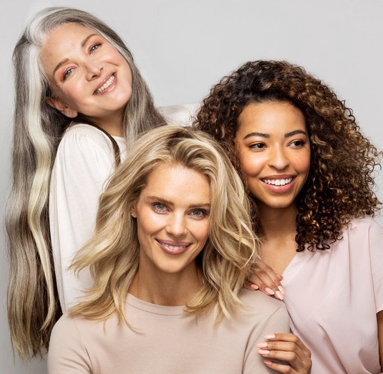 Drie lachende vrouwen met verschillende haarkleuren en -texturen: blond, grijs en bruin krullend.