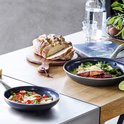 Deux poêles sur une table, l'une avec du saumon et du brocoli, l'autre avec des pâtes et des tomates.