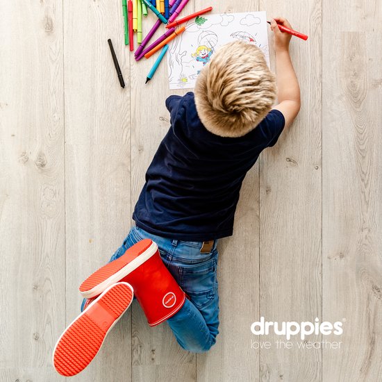 Jongen met rode laarzen met witte zolen, zittend op de vloer, tekent met stiften.