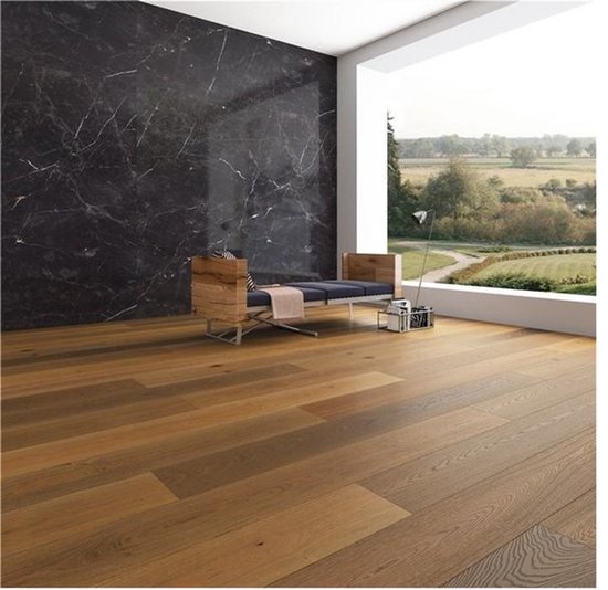 Houten vloer met warme tinten, liggend in een lichte kamer met een marmeren accentmuur en een moderne bank.