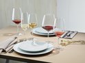Table dressée avec des verres à vin, dont certains remplis de vin rouge et blanc. Assiettes à motifs quadrillés.