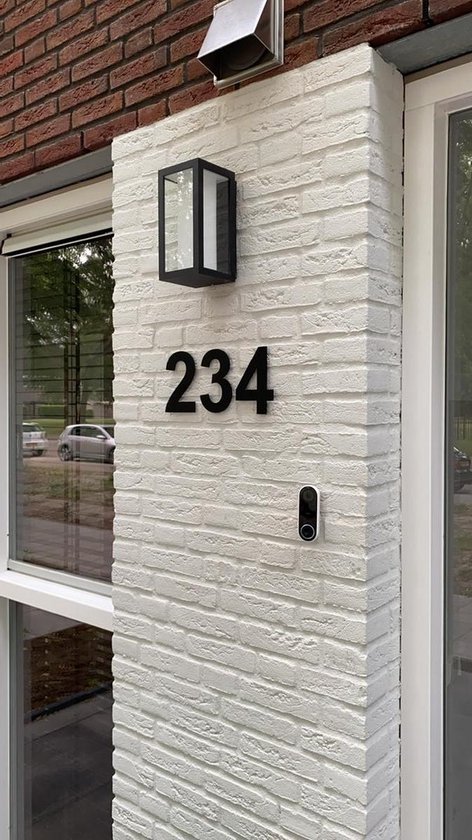 Huisnummer 234 in mat zwart, bevestigd op een witte bakstenen muur, naast een zwarte buitenlamp.