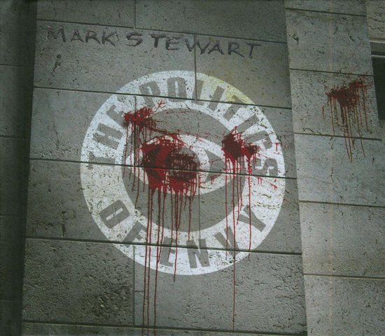 Een cirkelvormig wit logo met 'THE POLITICS OF ENVY' eromheen, besmeurd met rode verfspatten, op een stenen muur.