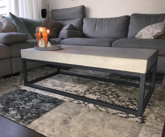 Betonnen salontafel met donkergrijs metalen frame op een vloerkleed in woonkamer.