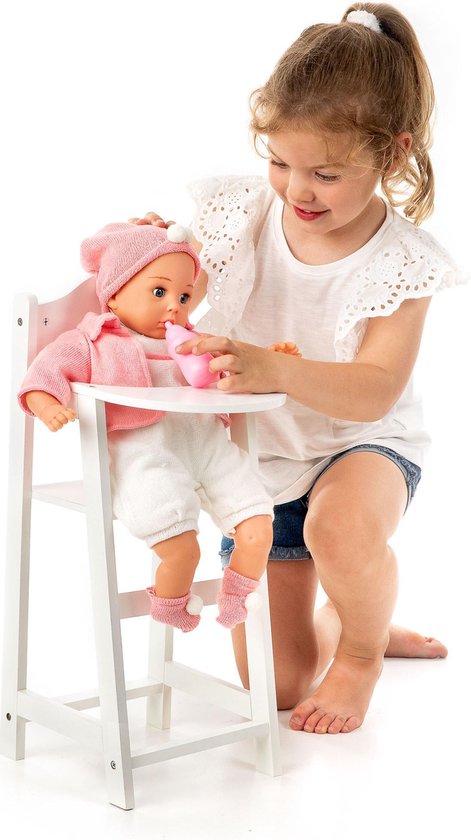 Meisje in witte top en spijkerbroek voedt een pop, gekleed in roze kleding, in een witte poppenstoel.