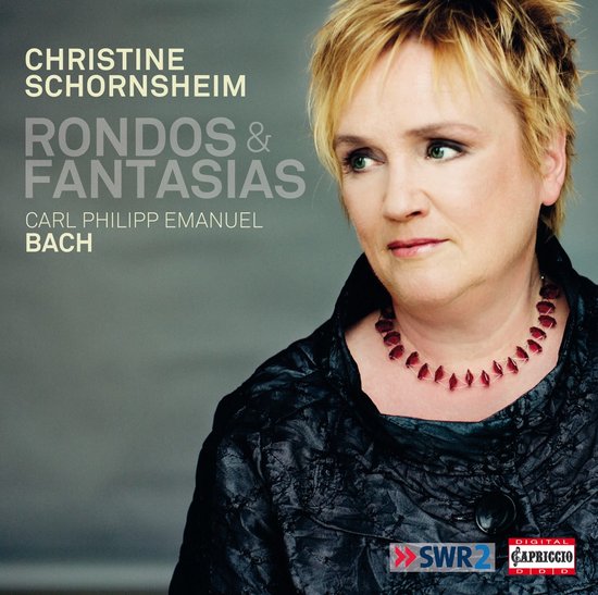 Christine Schornsheim, zangeres met blond haar, draagt een zwarte jas en een rode ketting.