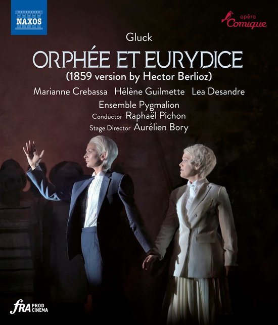 Twee vrouwen met kort blond haar, gekleed in een pak en een jas met rok, in een theaterproductie van "Orphée et Eurydice".