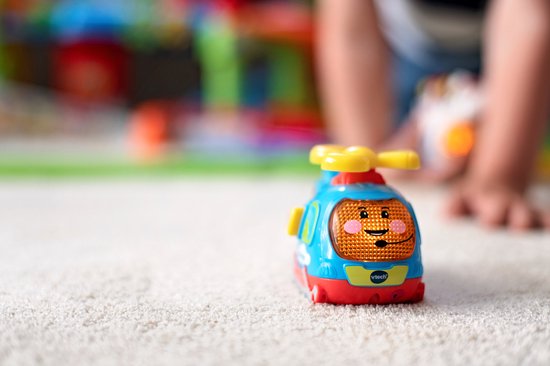 Hélicoptère bleu avec un visage et une hélice jaune sur un tapis doux. L'arrière-plan est flou.