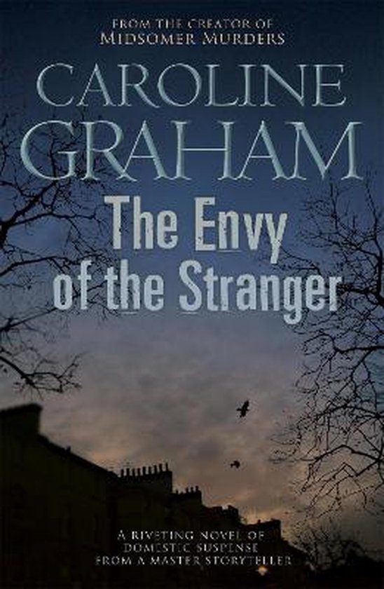 Boek kaft: "The Envy of the Stranger" van Caroline Graham, met silhouetten van gebouwen en bomen tegen een schemerige lucht.