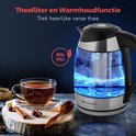 Glazen waterkoker met blauw verlicht water en theeblaadjes erin. Naast een kop thee.