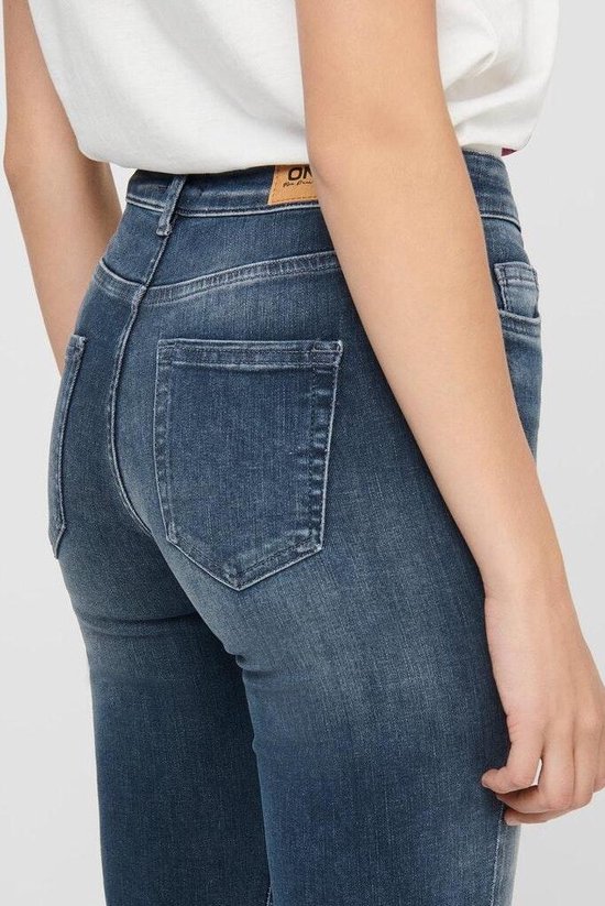 Close-up van de achterkant van een vrouw in een donkerblauwe skinny jeans met rafelige zoom. "ONLY" merklabel zichtbaar.