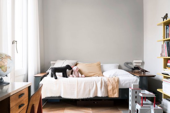 Kinderkamer met een bed, speelgoedhond en teddybeer, naast een gele boekenkast.