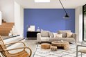 Een lichte woonkamer met een blauwe muur, een beige bank en rieten stoel.