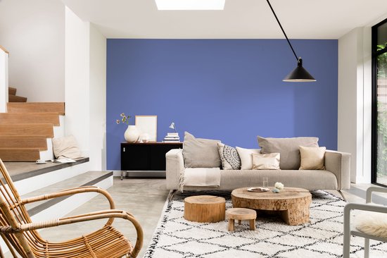 Een lichte woonkamer met een blauwe muur, een beige bank en rieten stoel.