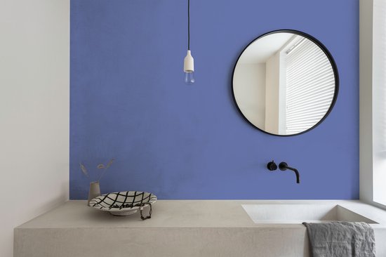 Een moderne badkamer met een blauwe muur, betonnen wastafel en ronde spiegel.