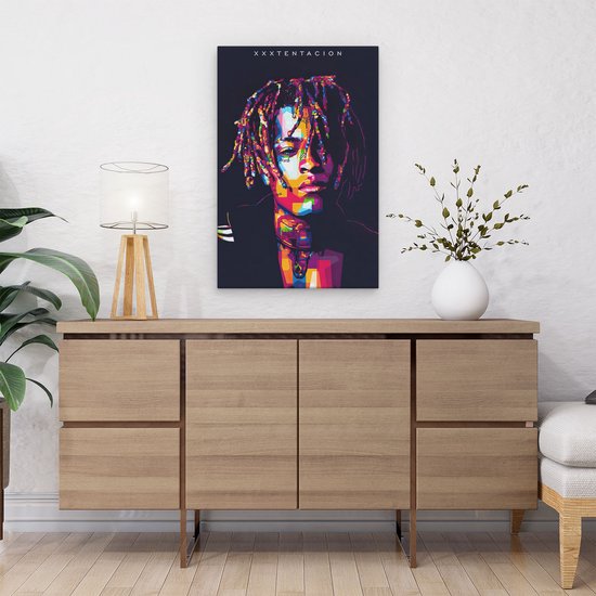 Abstract, kleurrijk portret van XXXTentacion op canvas, boven een dressoir met plant.