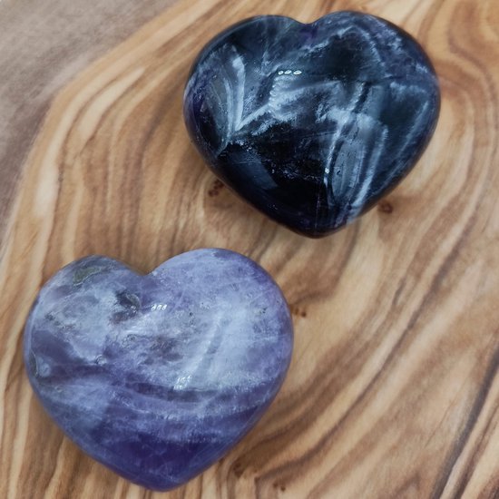 Twee amethist harten, paars met witte banden, op een houten ondergrond.