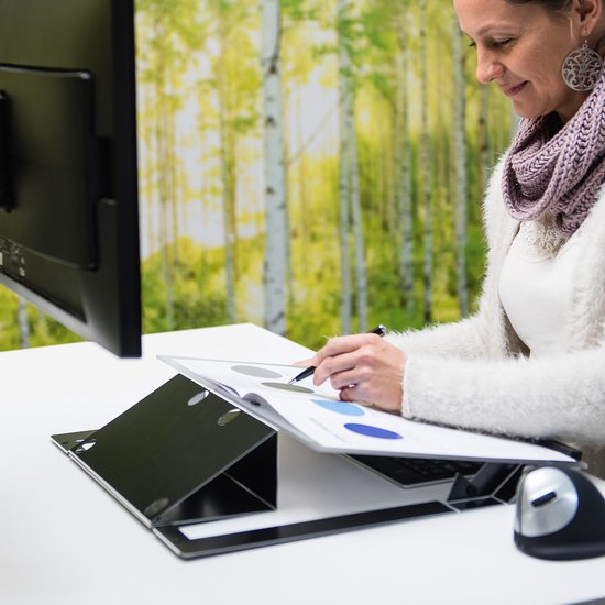 Zwarte documenthouder op een bureau met monitor, toetsenbord en muis. Een vrouw met een sjaal schrijft op een document.