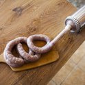 Een worstmakerij met een roestvrijstalen worstmachine die een opgerolde varkensdarm vult op een houten plank.