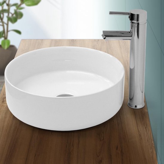 Witte, ronde keramieken wastafel met een chromen kraan op een houten blad.
