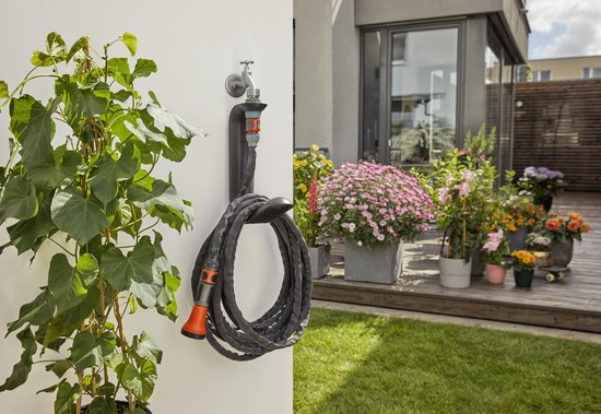 Zwarte Gardena Liano TapFix slanghouder aan een witte muur met kraan en een opgerolde tuinslang met oranje sproeikop.