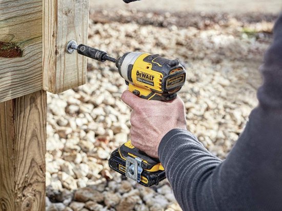 Hand met gele en zwarte DeWalt slagschroevendraaier die een schroef in een houten paal draait.