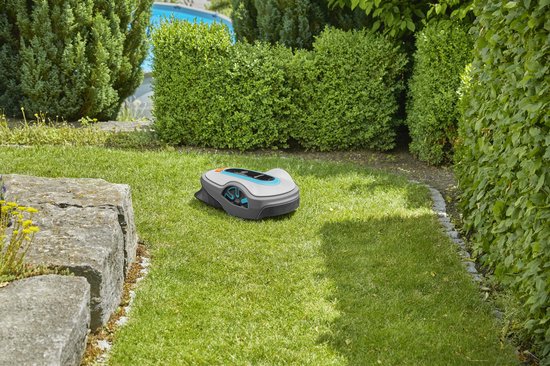 Grijze robotmaaier met blauwe en oranje accenten op een gazon, met struiken en een zwembad op de achtergrond.
