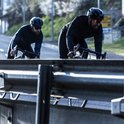 Twee mannen fietsen op een weg, beiden dragen zwarte fietsjacks.
