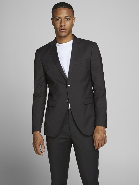 Jonge man met donkere huid draagt een zwart Jack & Jones blazer over een wit T-shirt en een zwarte broek.