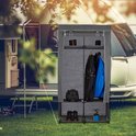 Grijze kledingkast met kleding, schoenen en kampeerspullen, in een buitenomgeving bij een caravan.