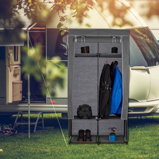 Grijze kledingkast met kleding, schoenen en kampeerspullen, in een buitenomgeving bij een caravan.