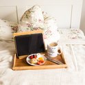 Ontbijt op bed met fruit, eieren, worstjes en koffie op een bamboe dienblad met tablet.