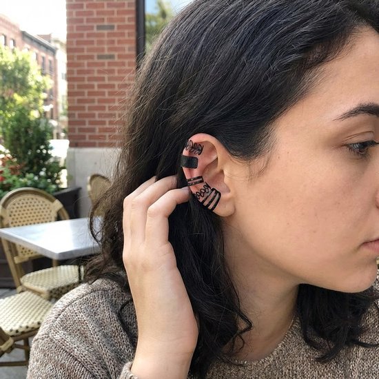 Model draagt zwarte oorclips met sierlijke, gebogen banden en een bladmotief op het oor.