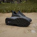 Zwarte Adidas Terrex trailrunningschoenen op een ondergrond van zand en gras, de ene schoen toont de zool.