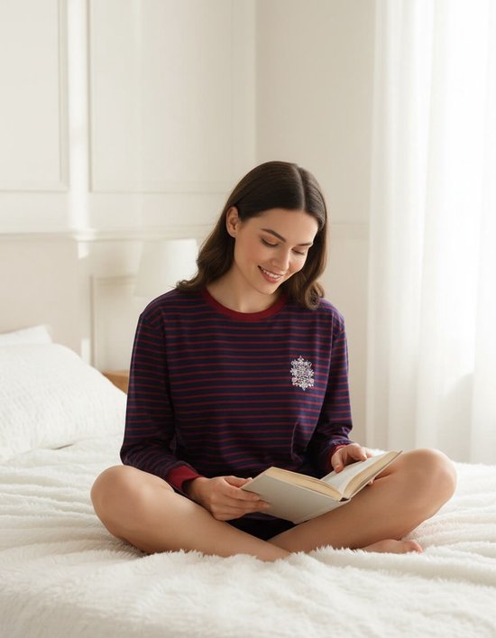 Een vrouw met lang bruin haar leest een boek in bed, zittend met gekruiste benen, in een donkerblauw gestreept nachthemd.