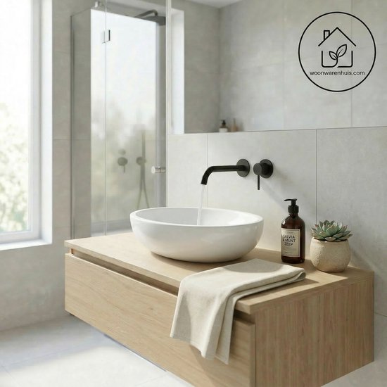 Een moderne badkamer met een witte, ovale waskom op een houten wastafelmeubel. Een zwarte kraan is gemonteerd.